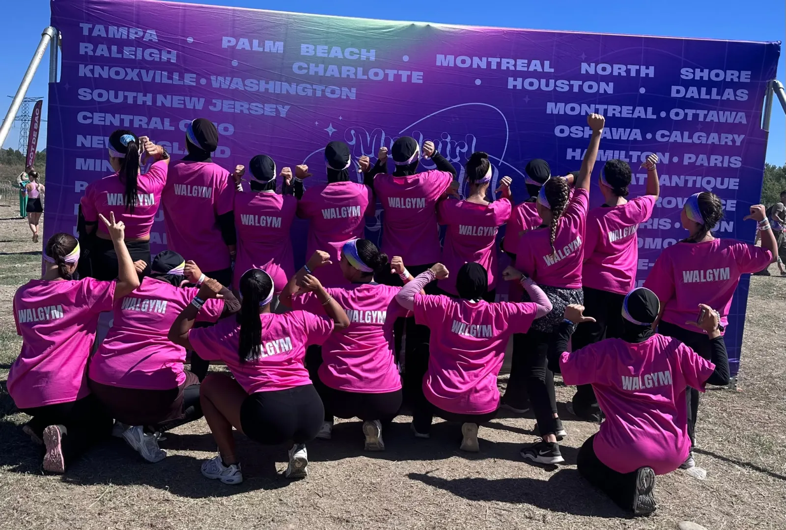 L'équipe Walgym de dos, en t-shirts roses Walgym, devant le panneau de la Mudgirl Run